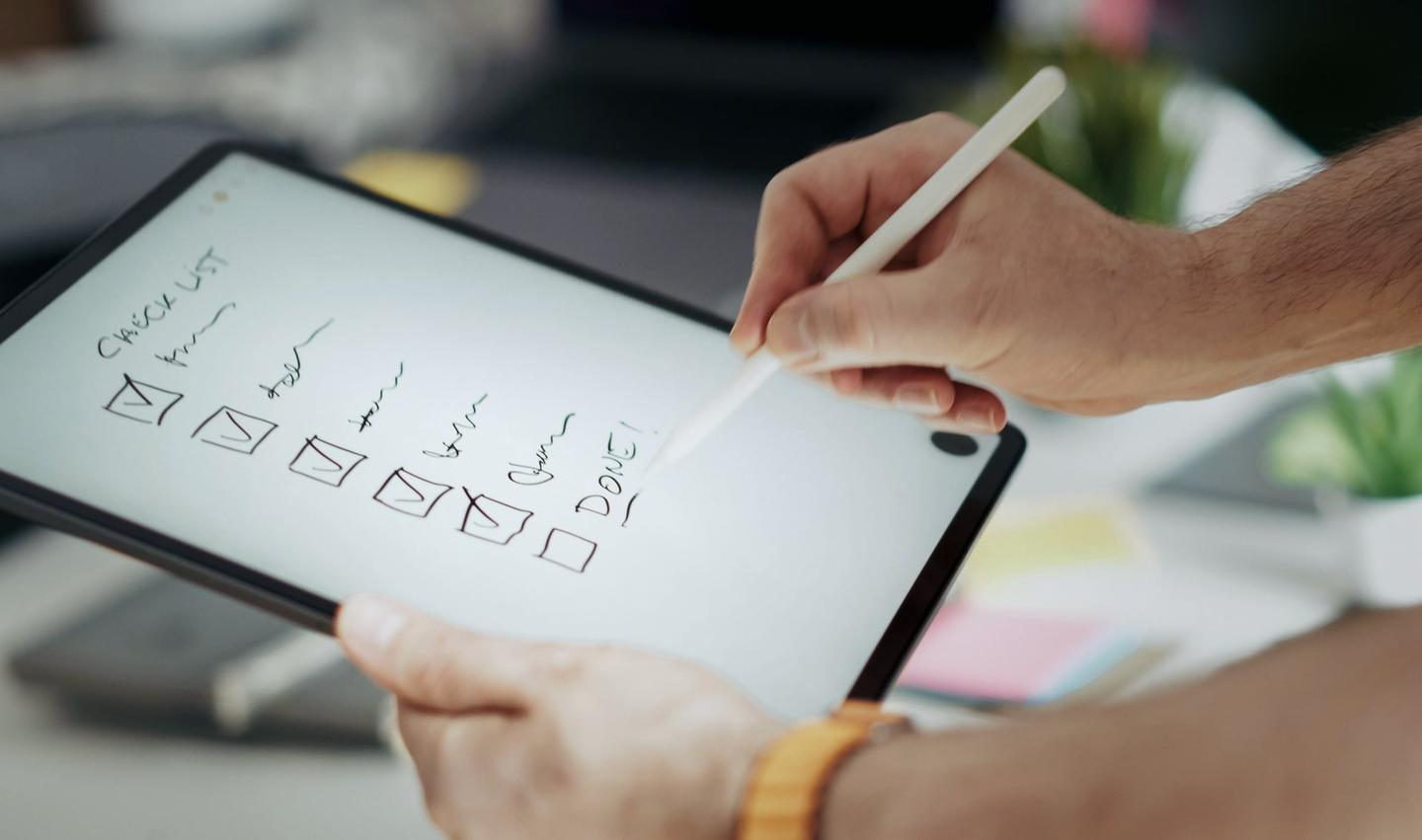 Hand hakt mit Stift eine Checkliste auf einem Tablet ab