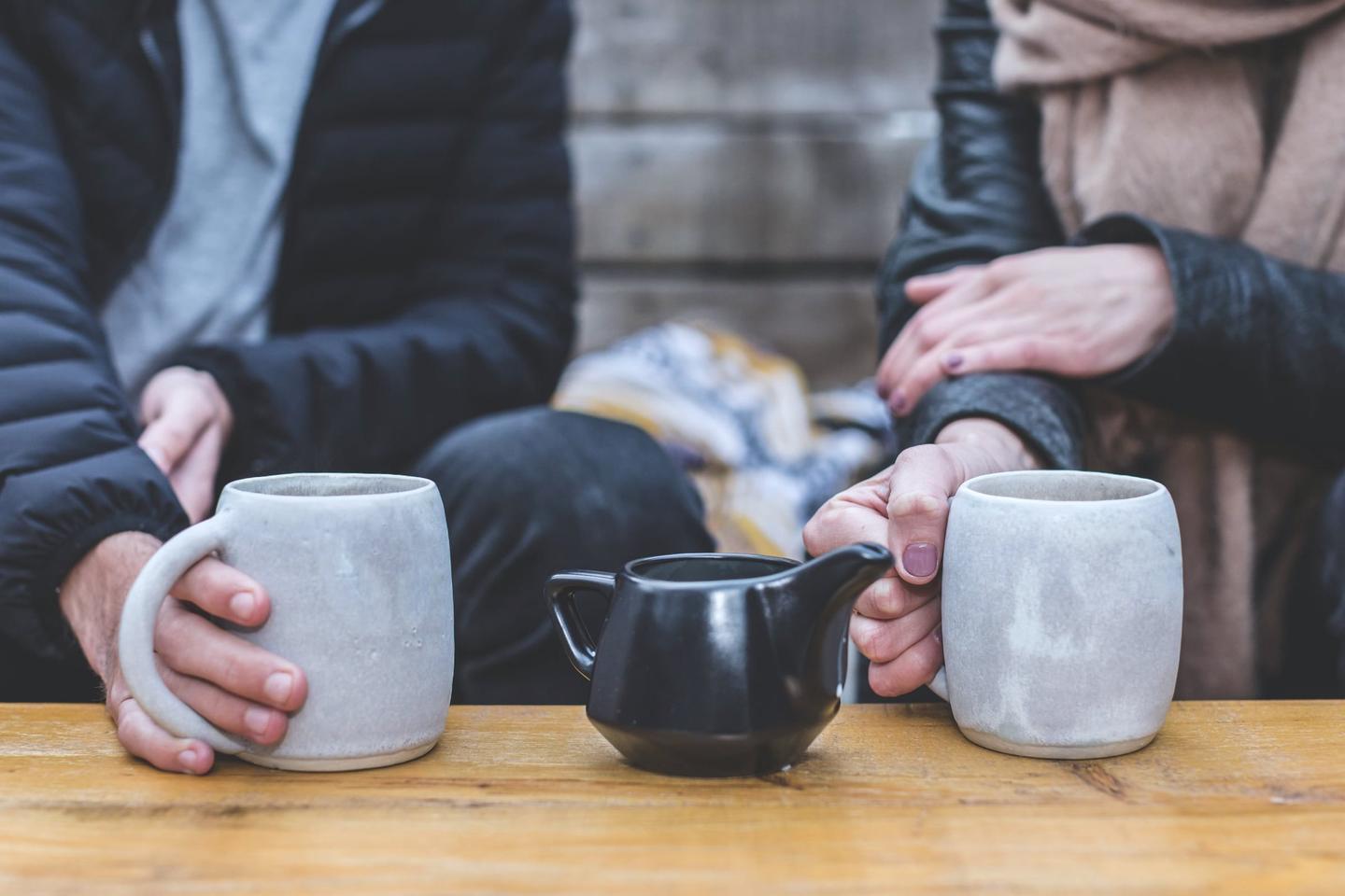 Zwei Personen im Gespräch am Tisch, Hände an Tassen